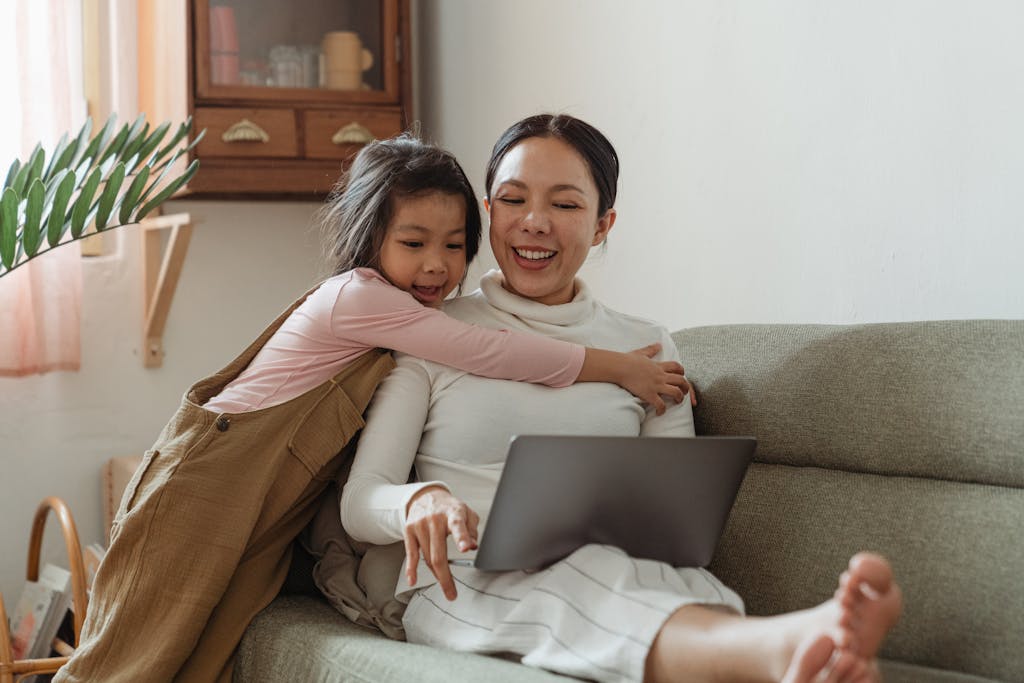 Cheerful girl hugging mother with laptop